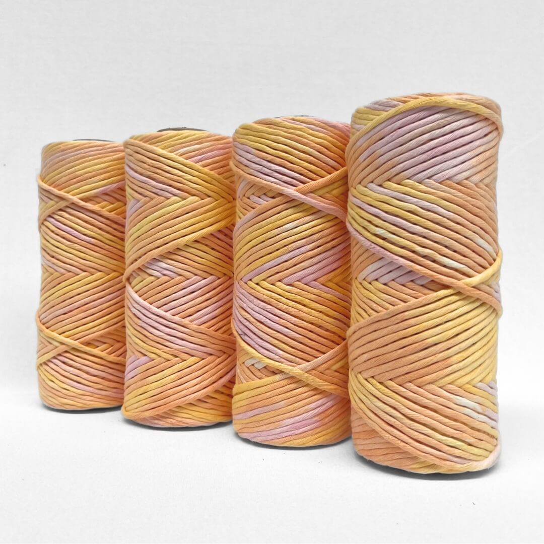 four rolls of sherbet hand painted string standing side by side angled on white background