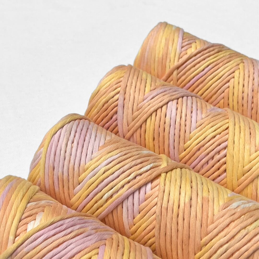 four rolls of sherbet hand painted string standing side by side angled on white background