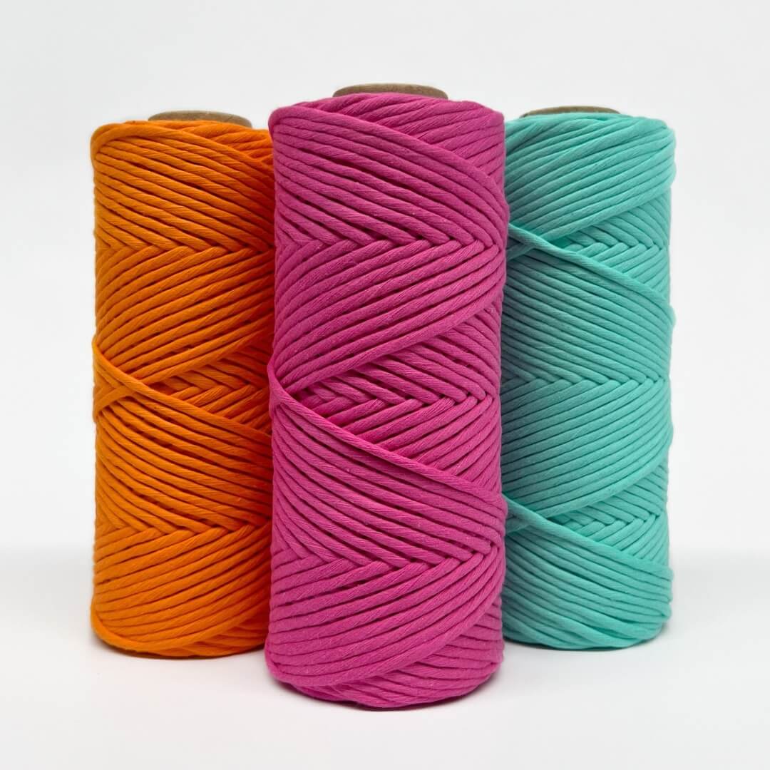 three rolls of neon macrame string in orange, pink and mint on white background