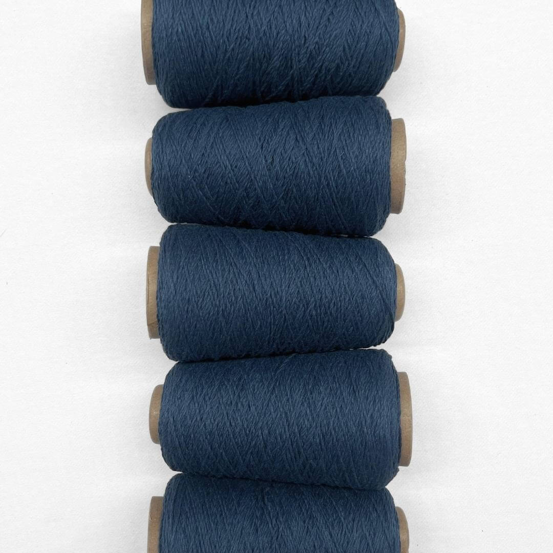 Navy Blue woollen yarn in flat lay showing five rolls of same colour laying side by side vertically down screen on white background showing up close texture