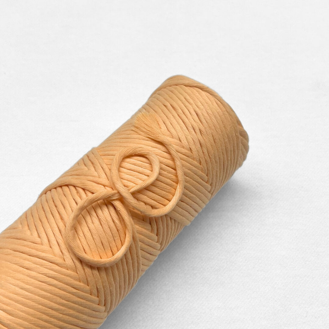 Soft pastel orange coloured roll of 4mm cotton string laying flat on white background with small brushed out section showing cottons softenss