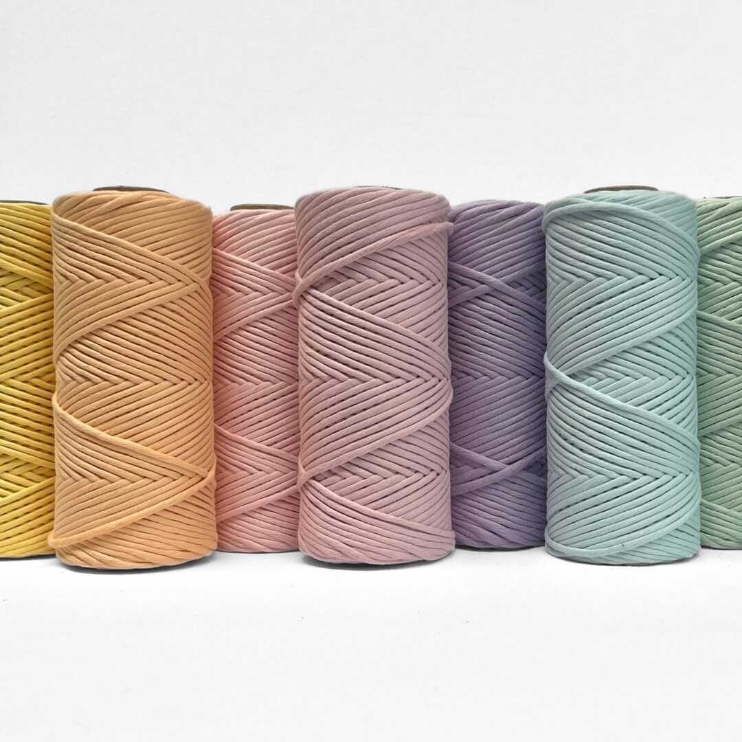 Soft pastel orange coloured roll of 4mm cotton string laying flat on white background with small brushed out section showing cottons softenss