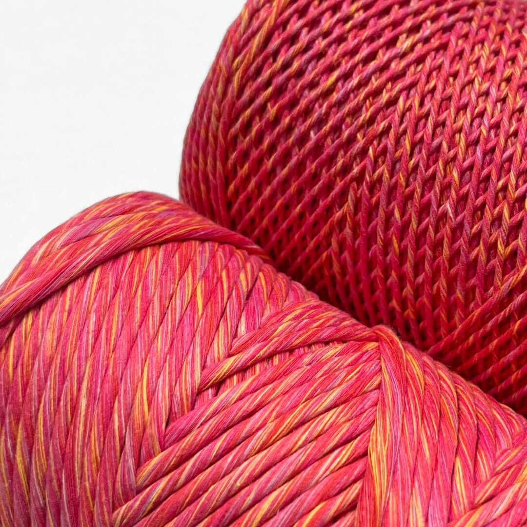 two rolls of sunburst macrame mixed string showing 1.5mm and 4mm variation pink yellow red colour way standing upright against white wall
