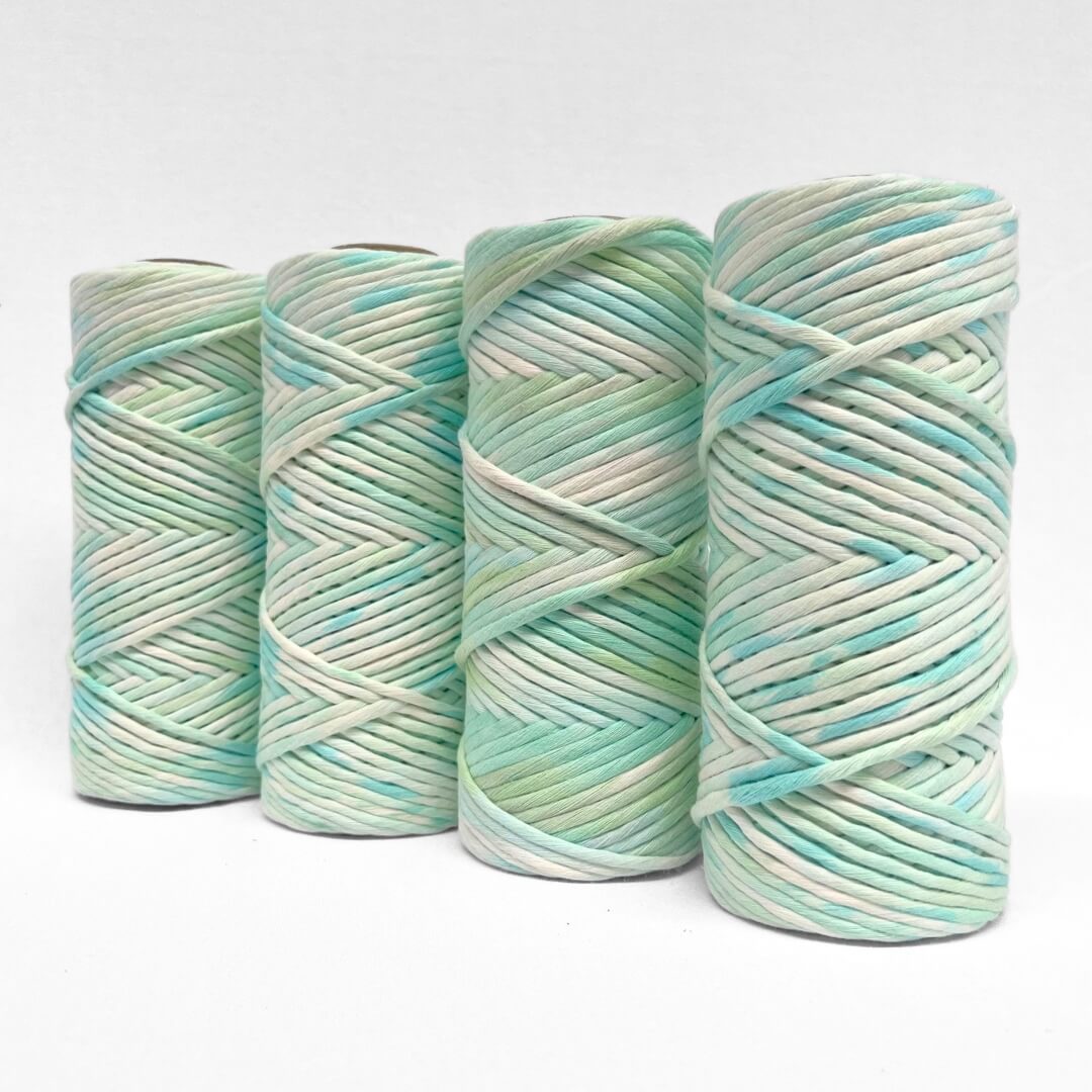 four rolls of blue and green hand painted macrame string standing upright on white background
