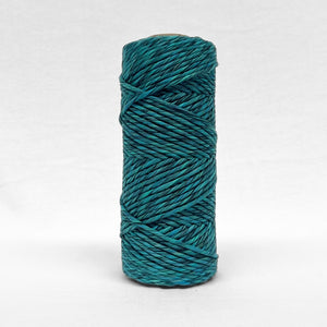 one roll of 4mm cotton mixed string in colourway aura blue a combination of blue green and black standing upright on white backdrop