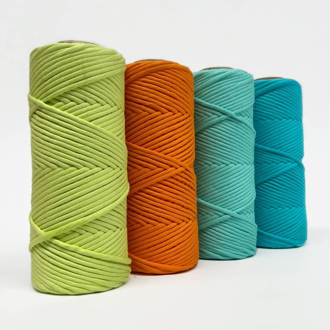 four rolls of neon macrame string in neon green, orange, and blue, standing side by side on white background