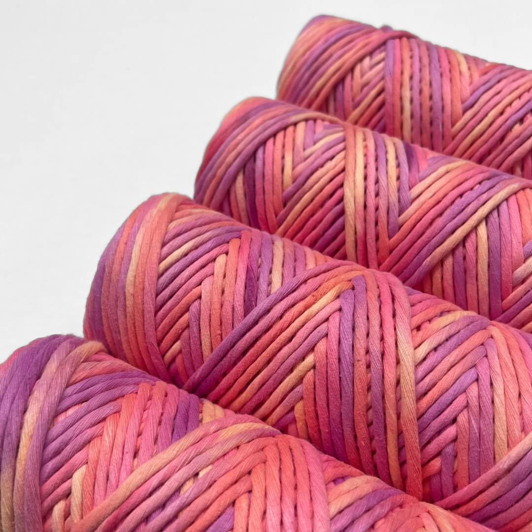 four rolls of hand painted string on coral reef colour way consisitng of coral, pink,purple and yellow stand upright on white background