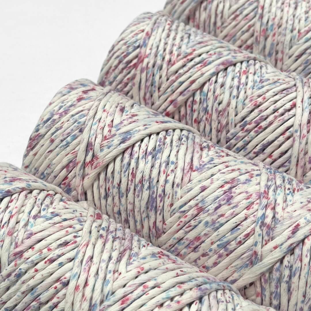 four rolls of pink purple and blue specklied cotton string standing side by side on white background