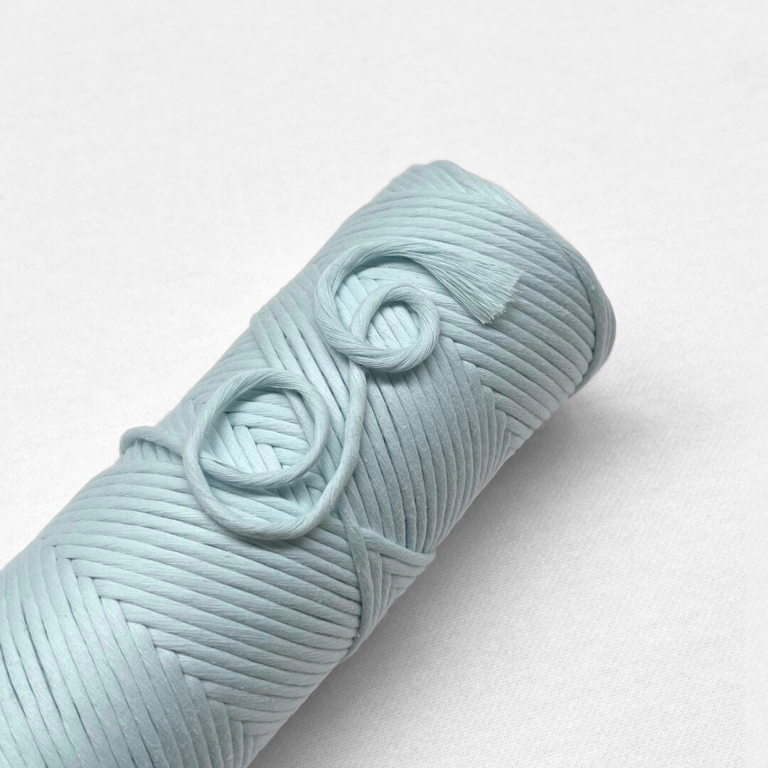 one roll of cototn amcrame cord in pastel blue colour laying flat on white background 