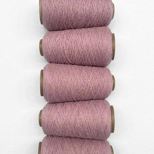 Five rolls of primrose pink wool yarn side by side in flat lay on white background