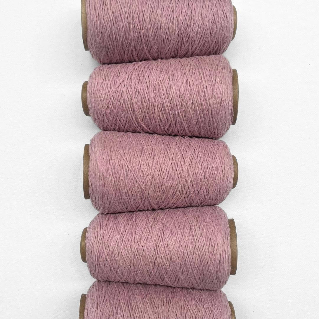 Five rolls of primrose pink wool yarn side by side in flat lay on white background