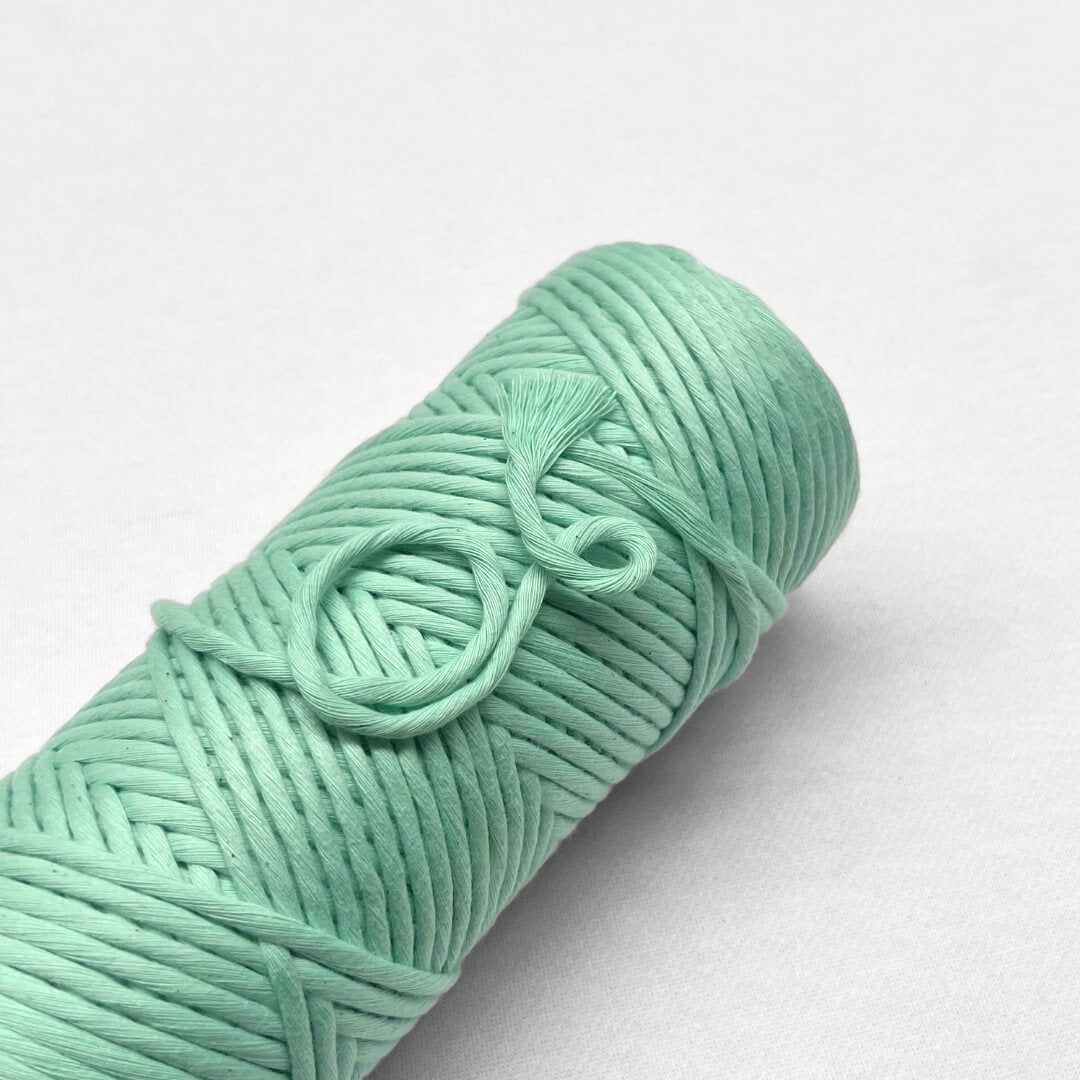 one roll of spring green pastel amcrame cord laying flat on white wall with small brushed out section showing cotton softness