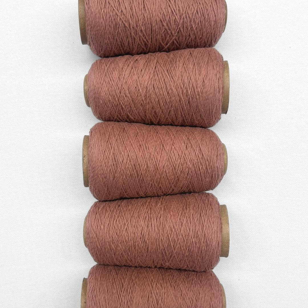 Five rolls of rose tea woolen cord laying next to each other vertically in image on whit background