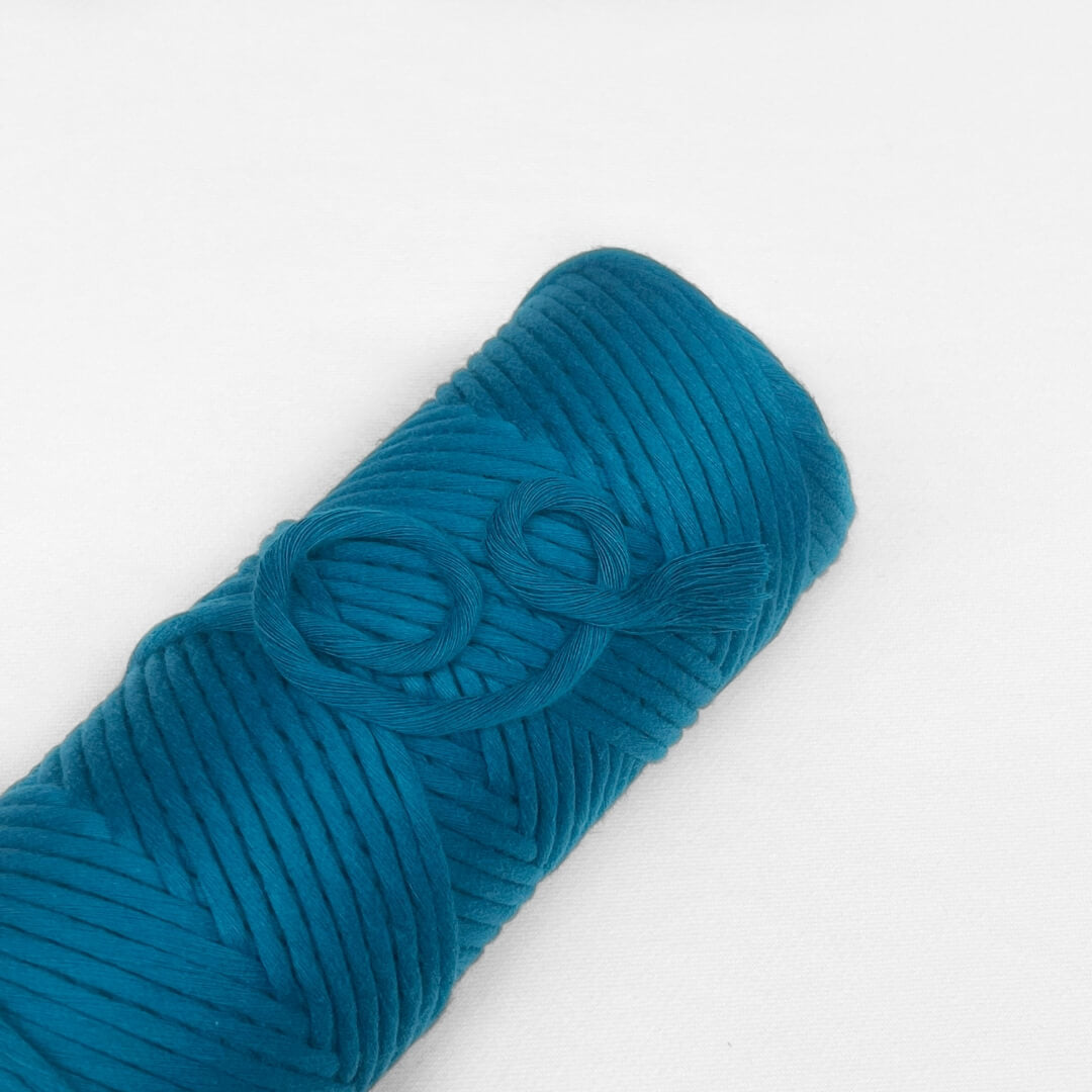 one roll of cotton cord for macrame weaving diy craft in colour mykonos blue laying flat and angled on white background