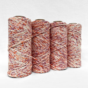 four rolls of flora fiesta cotton string made up of purple and orange standing side by side with white background