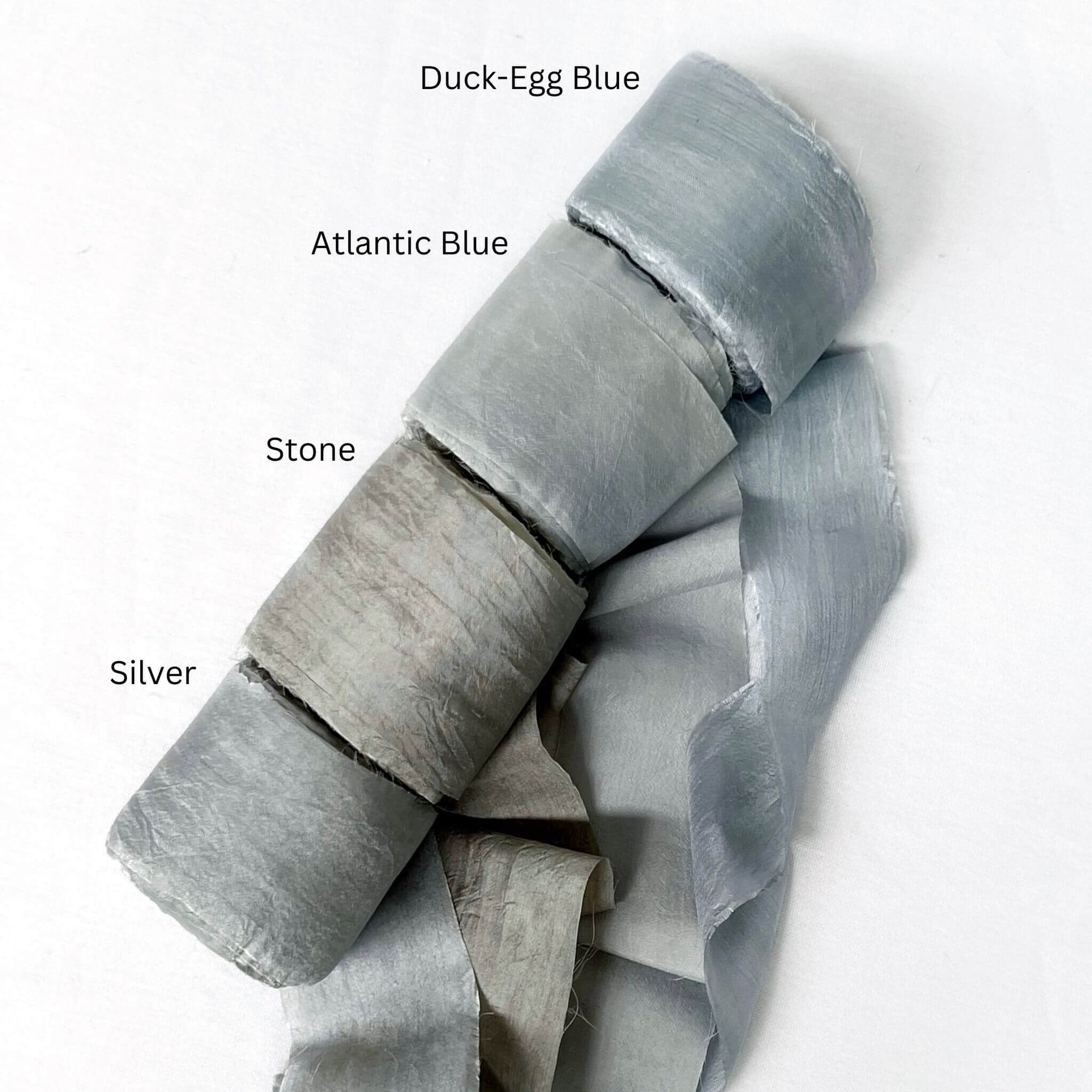 soft blue duck egg atlantic stone grey silver grey wide silk ribbon rolls for luxury gift wrapping on white wall 