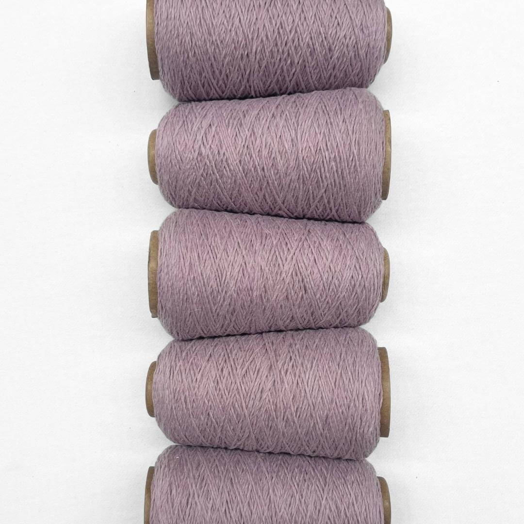 Five cones of iced lilac wool cord laying flat and side by side on white back ground