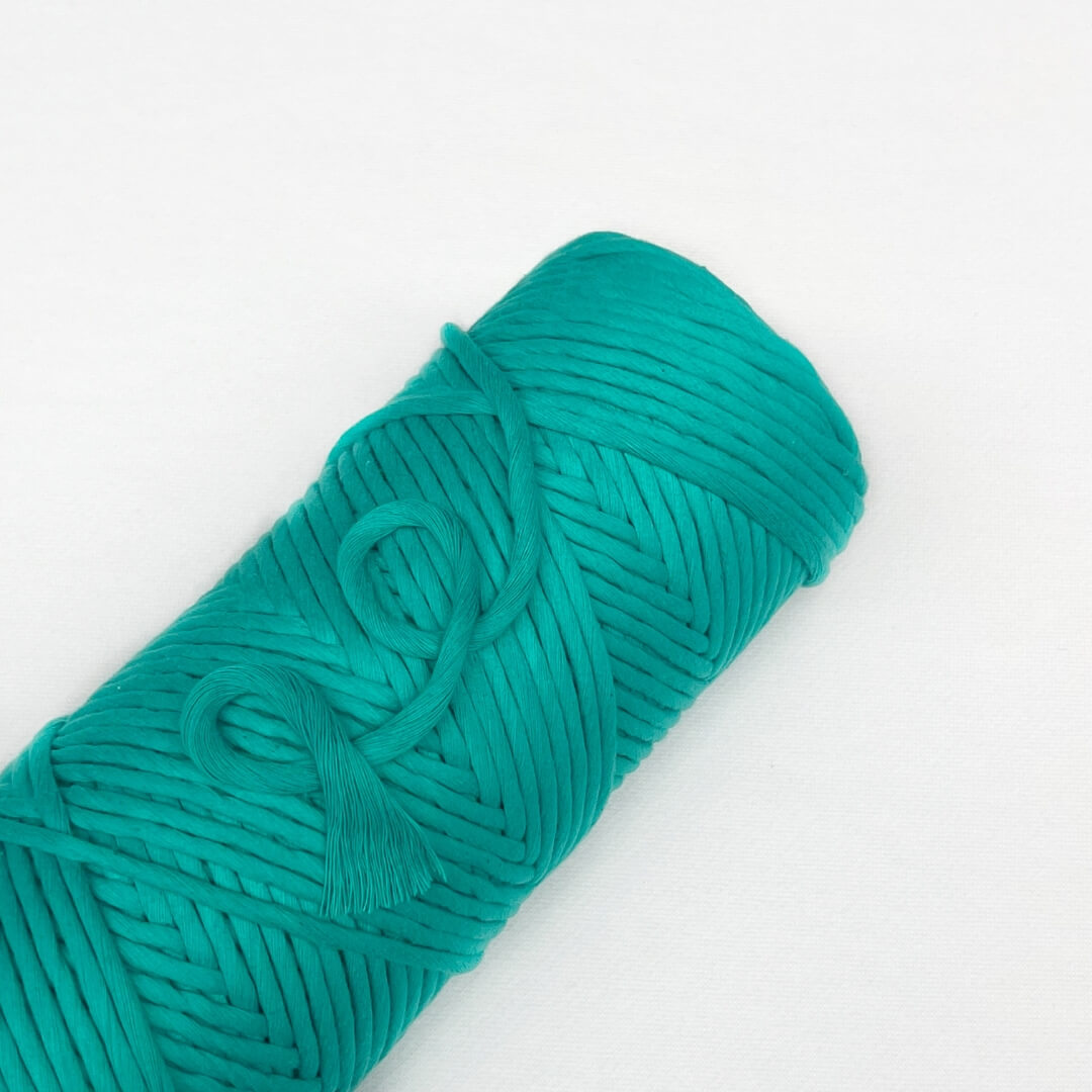 roll of turquoise cloud 9 cotton string laying flat and angled on white background small brushed piece demonstrating soft texture of the string