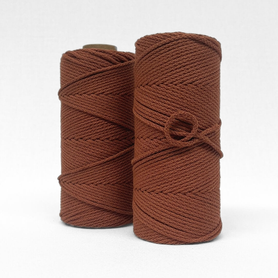 two rolls of rust brown cotton cord standing side by side on white backdrop