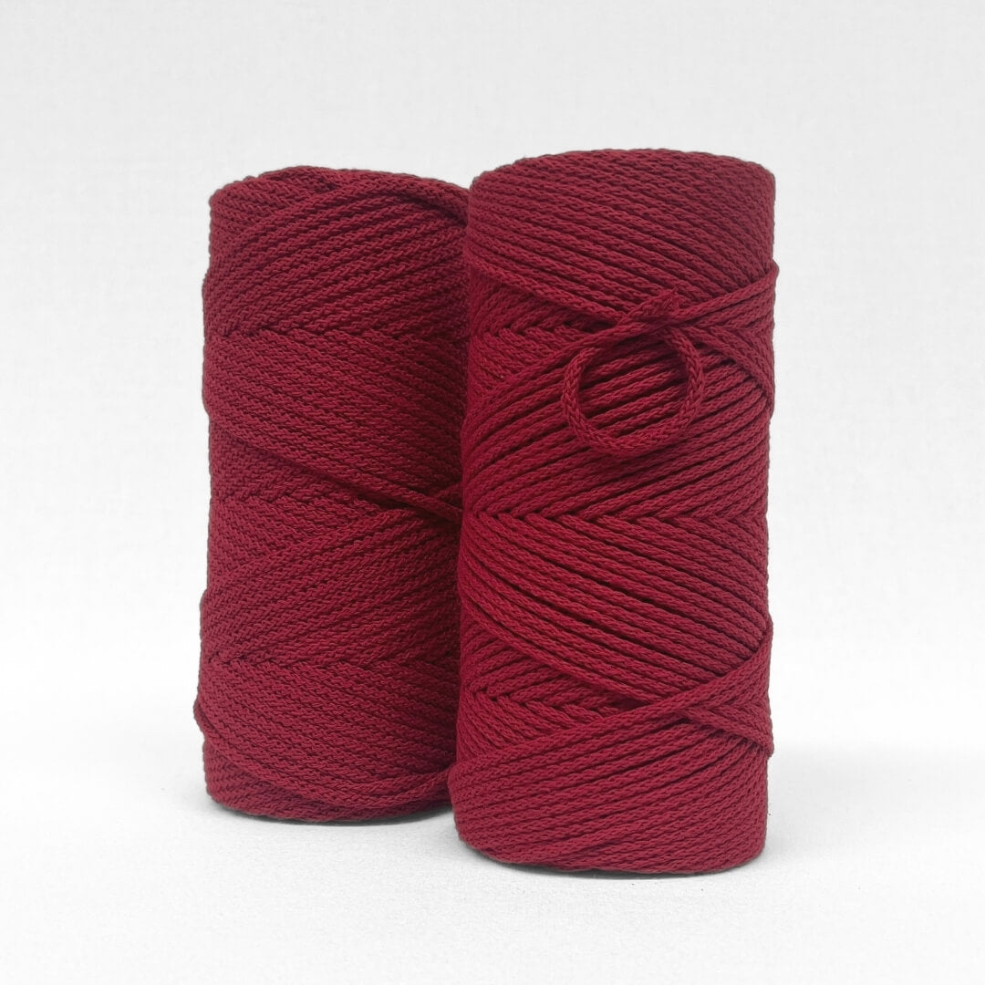 two rolls of 4mm braided cotton cord in chilli red standing side by side on white back drop