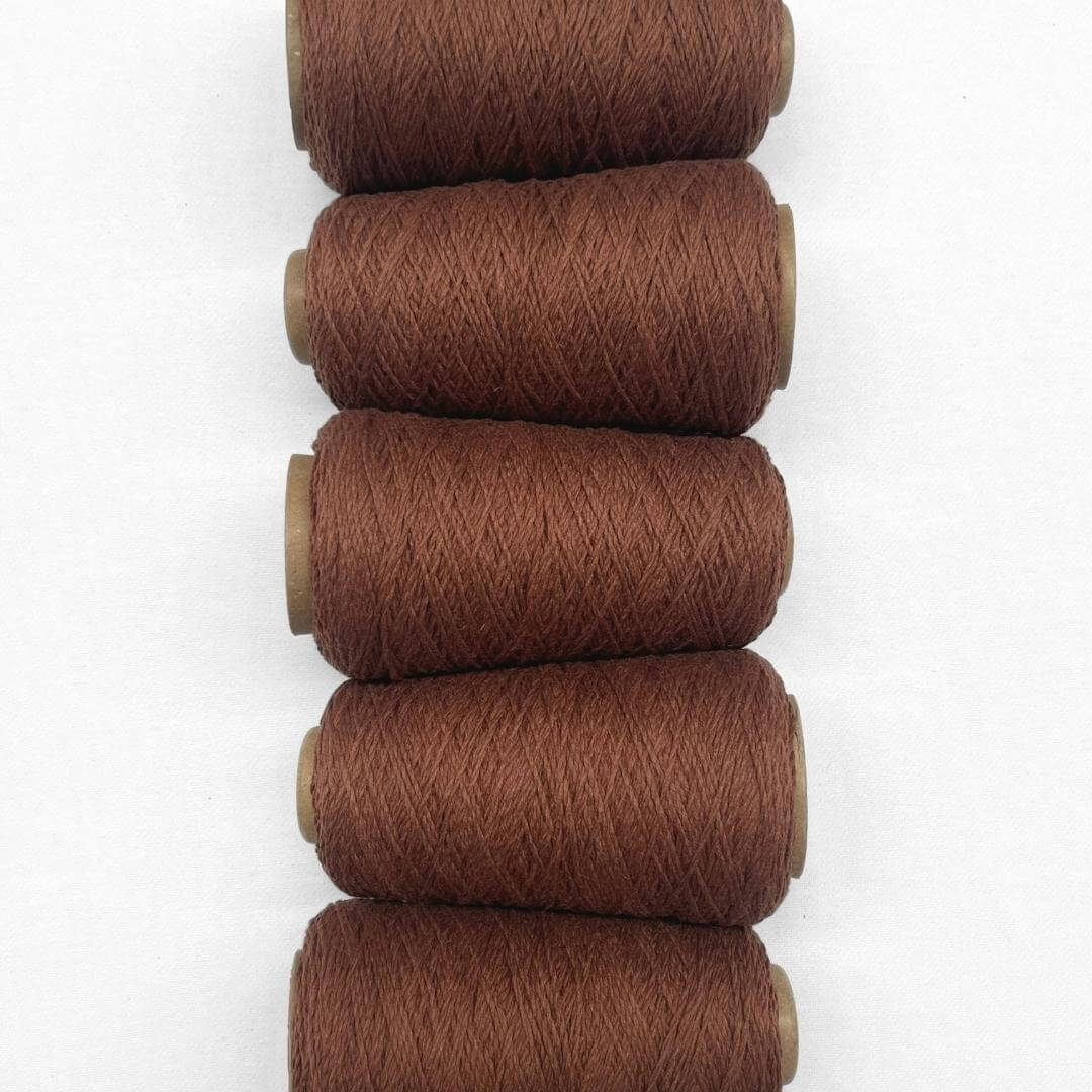 5 cones of rust brown woolen yarn laying side by side on white background showing up close softness