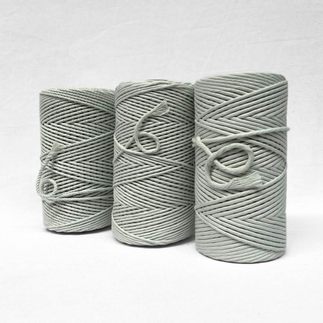 three rolls of cotton standing next to each other on an angle in different sizes and muted green colour on white background