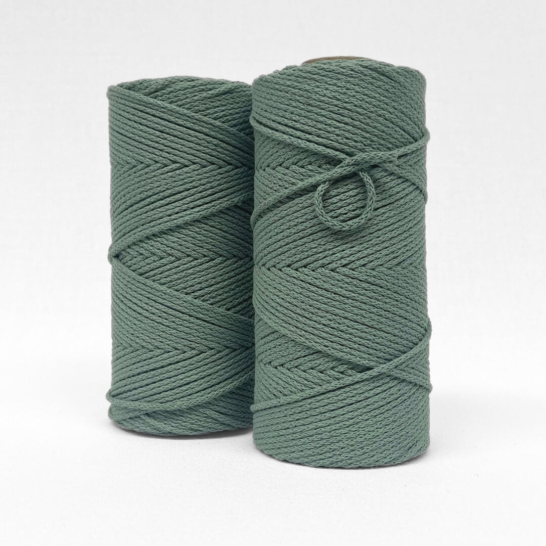 two rolls of sage green braided cotton macrame cord on white wall