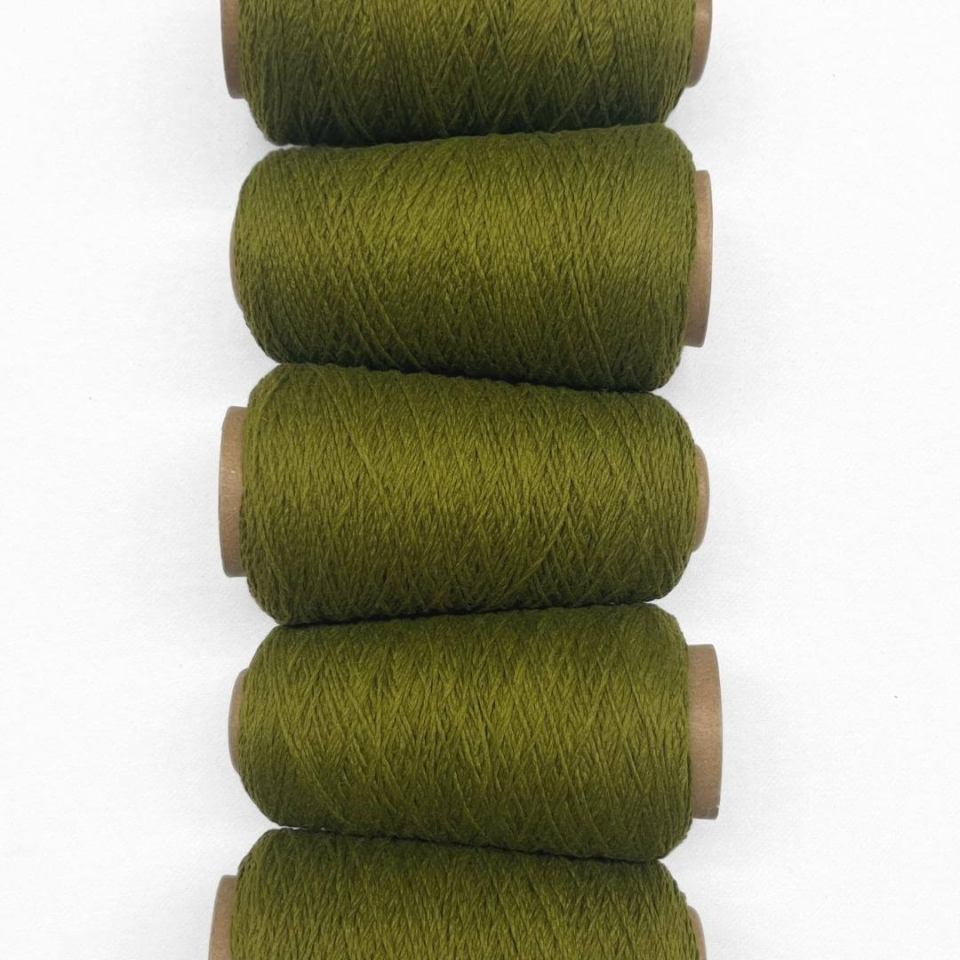 Olive green woll yarn in flat lay showing five rolls of same colour laying side by side on white background