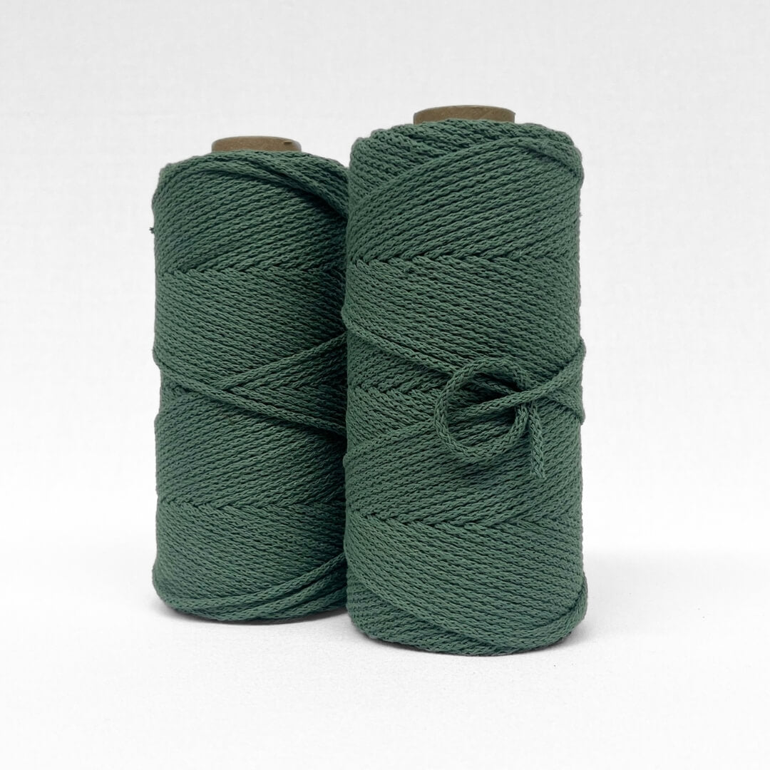 two rolls of braided 4mm cotton cord in ivy green standing side by side on white wall