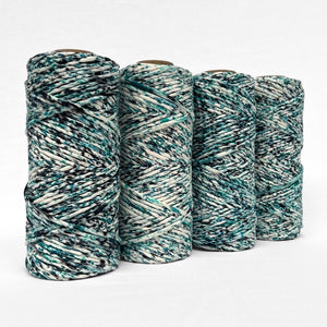 image of four rolls of confetti cotton cord in aura blue made up of deep blue green and black specks on a white base standing side by side on white wall