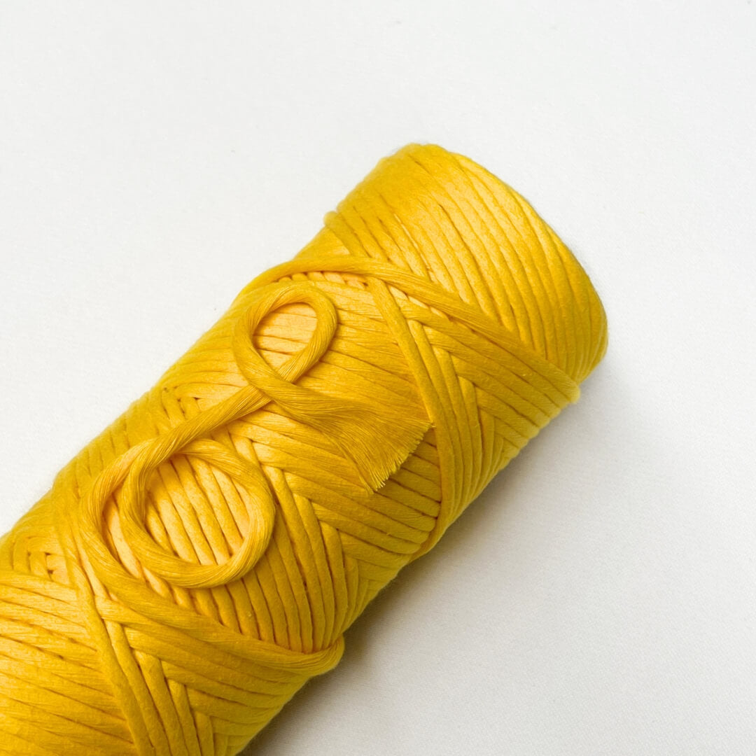 one rolls of cotton macrame cord in daffodil yellow laying flat on white background with small brushed out piece showing soft texture