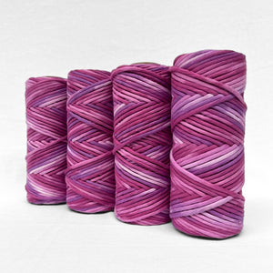 four rolls of very berry purple hand painted cloud 9 macrame cord standing upright and angled on white wall 
