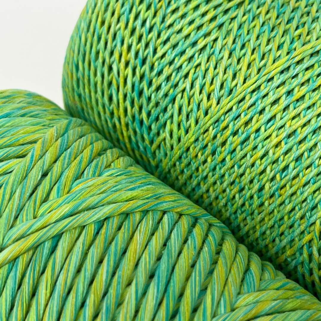 Two rolls of green, yellow and blue mixed macrame string standing up on white background