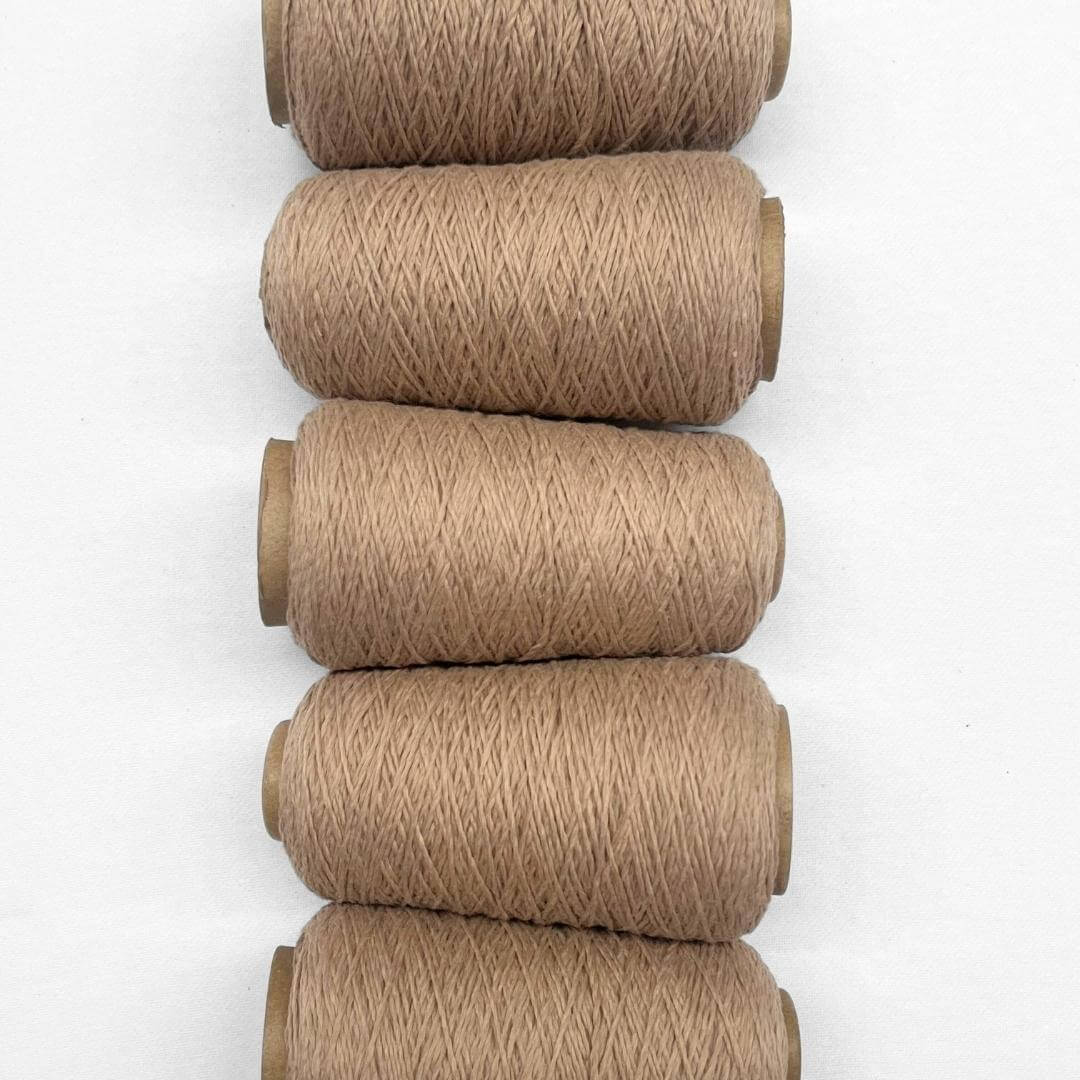 Five rolls of soft brown woolen yarn laying side by side vertically on white backdrop