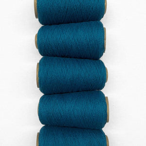 5 rolls of deep mykonos blue woolen yarn in flatlay image laying side by side on white background