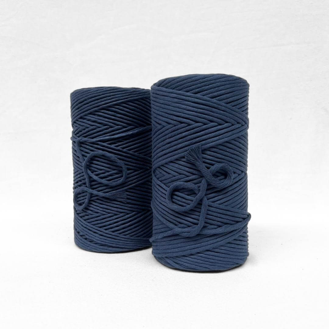 two rolls of navy blue cotton string standing on angle on white background