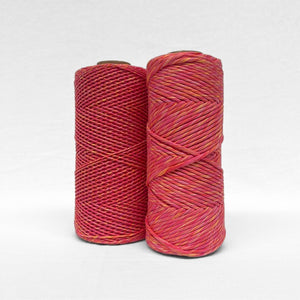 two rolls of sunburst macrame mixed string showing 1.5mm and 4mm variation pink yellow red colour way standing upright against white wall
