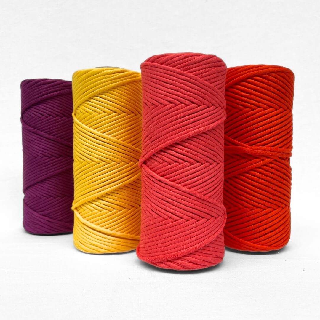 four rolls premium macrame cotton cord showing vibrant purple yellow watermlon and flame orange all standing up on white backdrop
