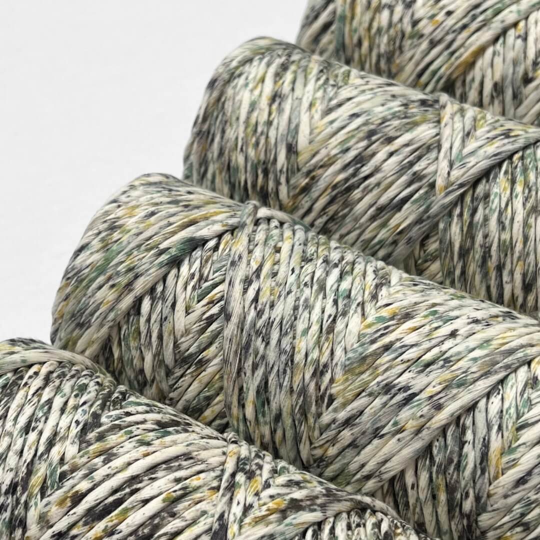 four rolls of green yellow black spotted macrame cord laying flat showing up close colour application on white background