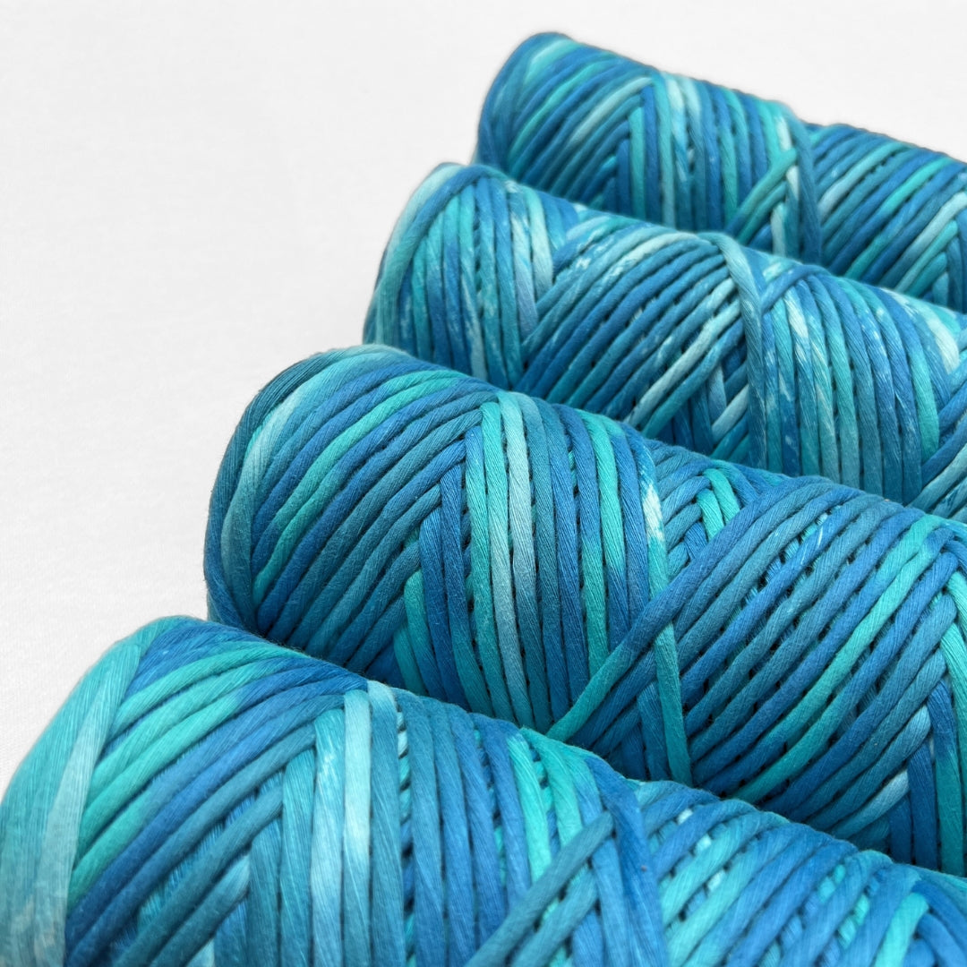 four rolls of hand painted cotton cord in blue and green colour way called ocean breezed standing upright on angle on white background 