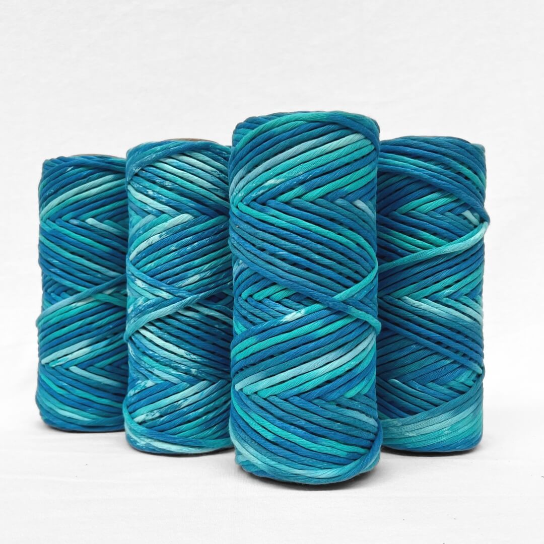 four roll of hand painted luxury macrame cord in blue and green colour melt standing upright on white wall 