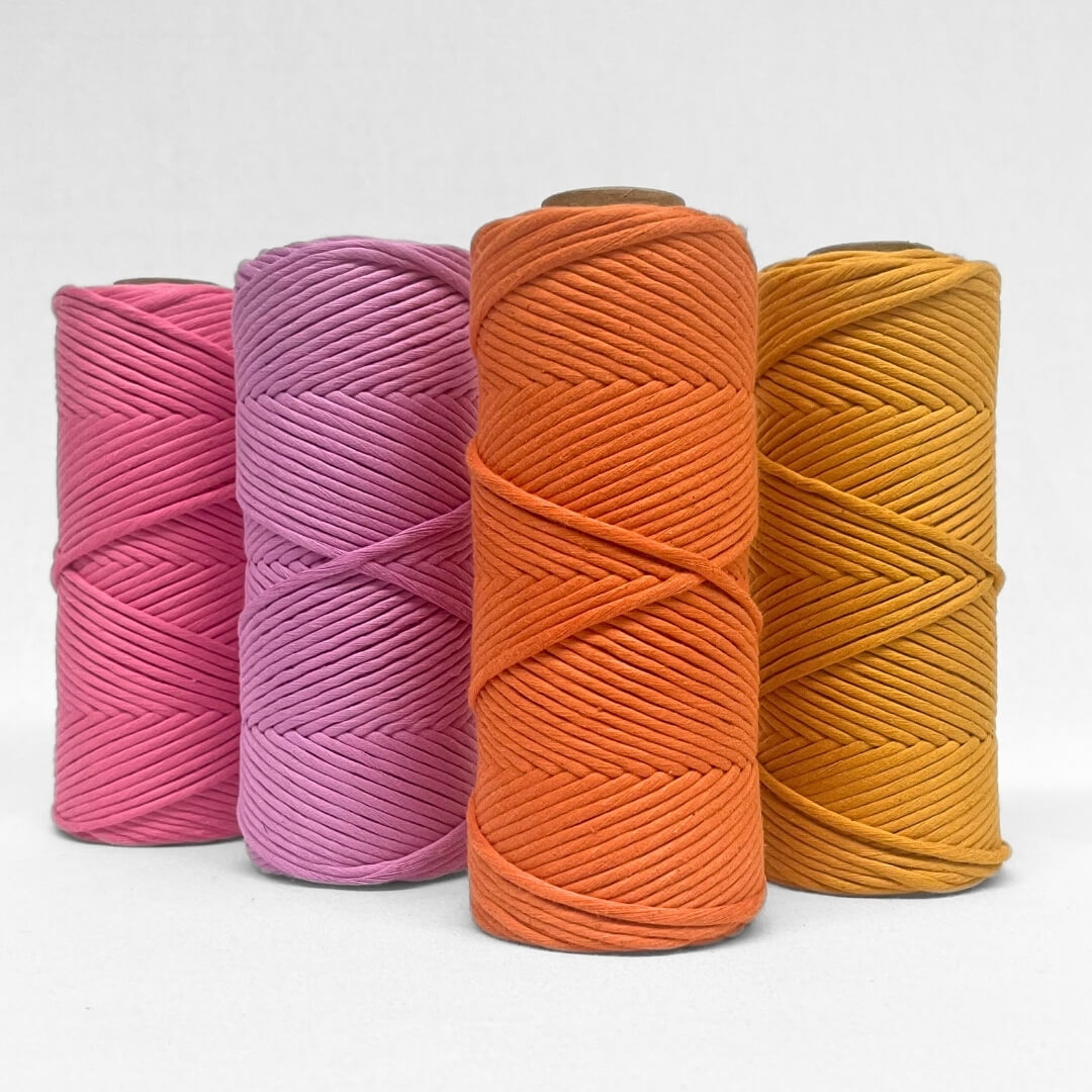 four rolls of cloud 9 string in pink power, vivid violet, orange zest and mellow marigold, standing on white back drop