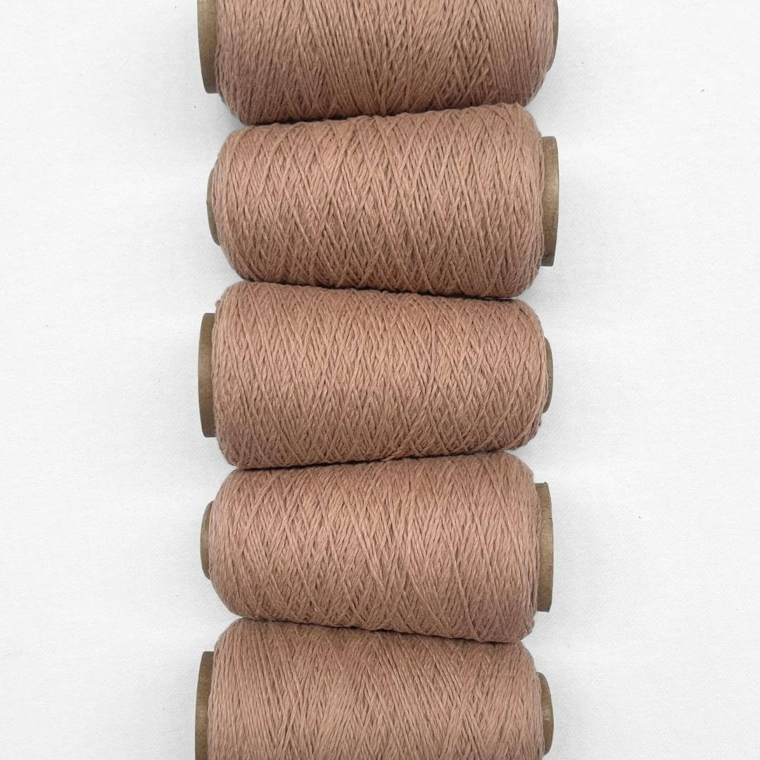 Five cones of muted peach wool cord laying flat vans vertical on whtie background