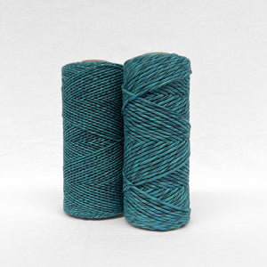 two rolls of vibrant mixed cotton string made from blues green and black one 1.5mm and one 4mm standing side by side on white background