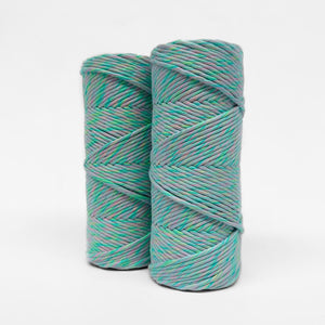 two rolls of bright rainbow mixed macrame string standing upright on white background