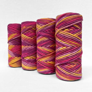 four rolls of hand painted cotton string in electric sunset colour way made up of vibrant pink purple yellow standing side b side on white background 