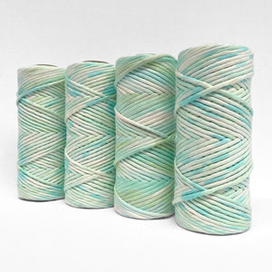 four rolls of blue and green hand painted macrame string standing upright on white background 