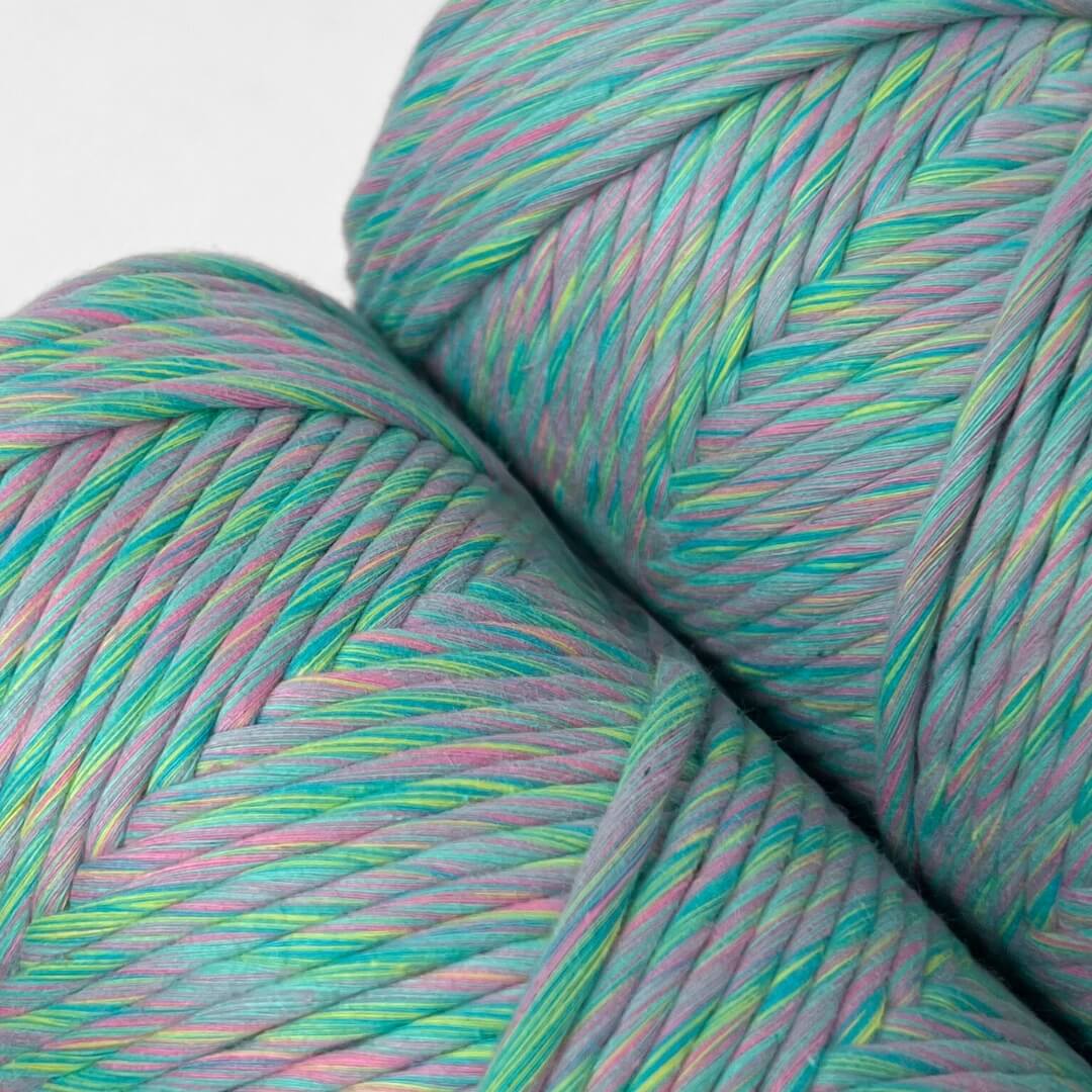 two rolls of bright rainbow mixed macrame string standing upright on white background