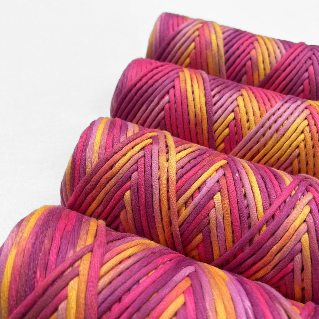 four rolls of hand painted cotton string in electric sunset colour way made up of vibrant pink purple yellow standing side b side on white background 