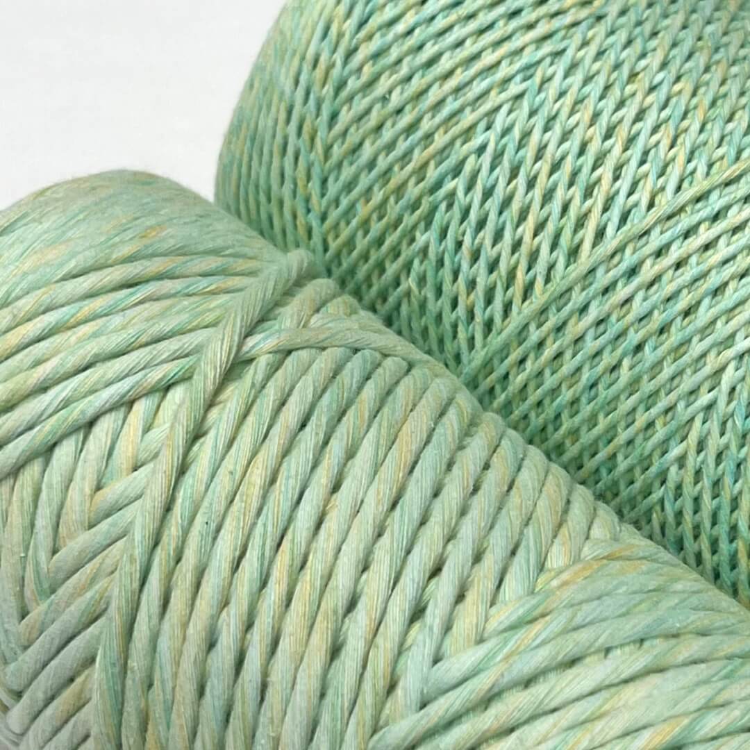 two rolls of lime splice cotton macrame ixed string standing sie by side on white background in 4mm and 1.5mm variants